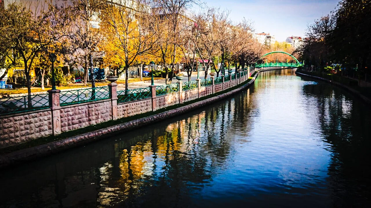 Eskişehir Porsuk kenarında ağaçlar ve su yansımaları, Eylül 2021; şehir ortamı, restoran masası veya güncel tekne seferi belgesi değildir.