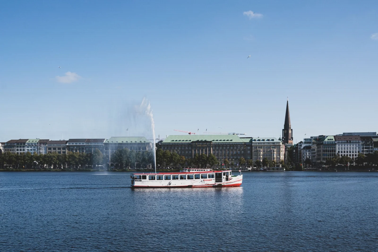 A boat, fountain and city skyline on Hamburg Alster Lake