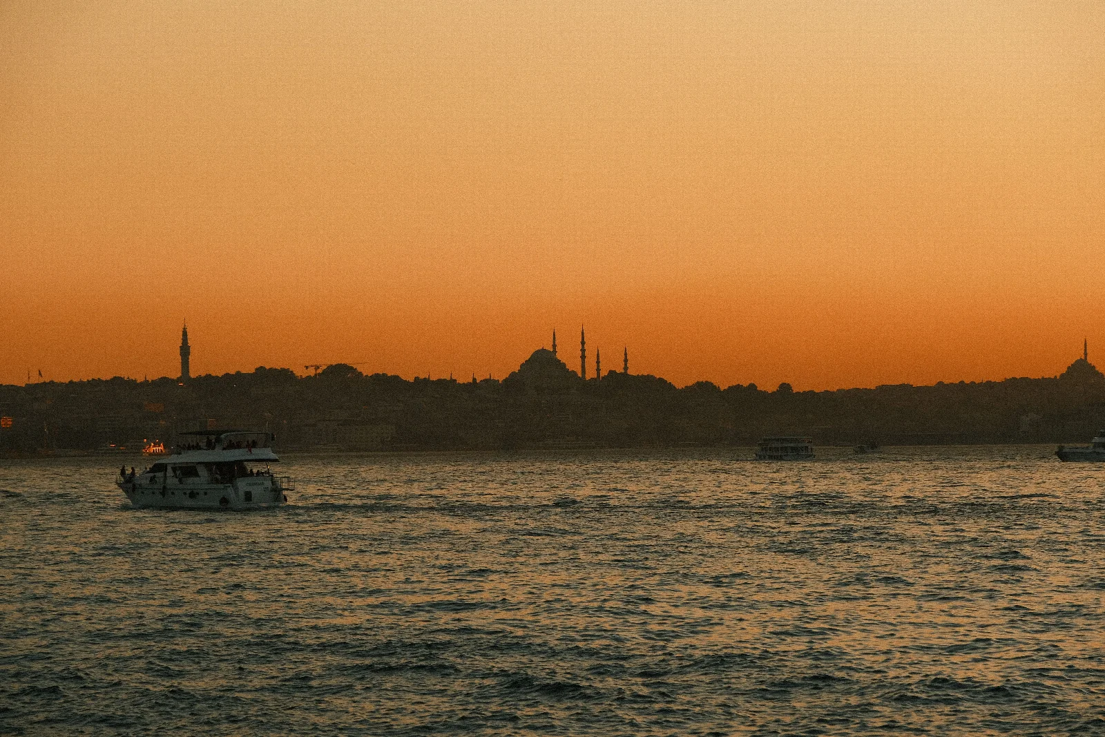 Gün batımında İstanbul’un kubbeli silueti, turuncu gökyüzü ve su üzerindeki tekneler