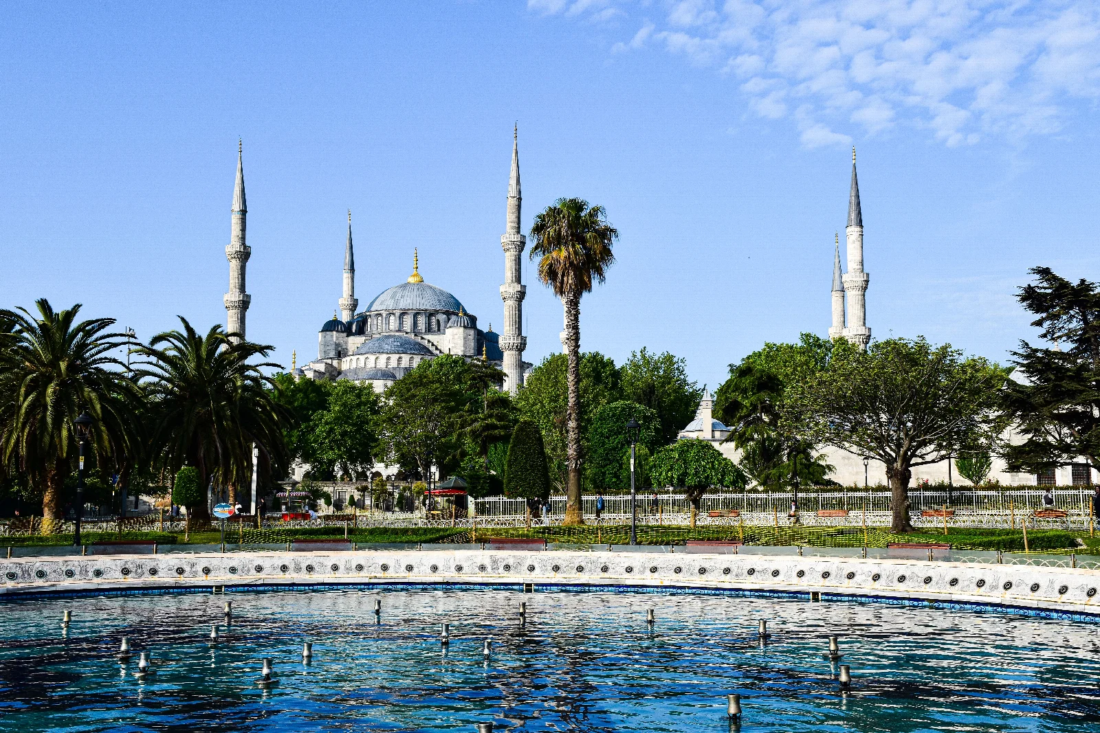 Sultanahmet Camii’nin kubbeleri ve minareleri, yeşil ağaçlar ve ön plandaki süs havuzu