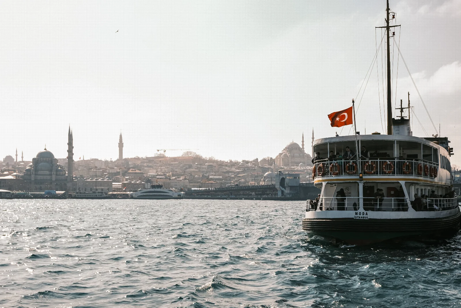 İstanbul’da Türk bayraklı beyaz vapur, dalgalı su ve arka planda tarihî cami silueti