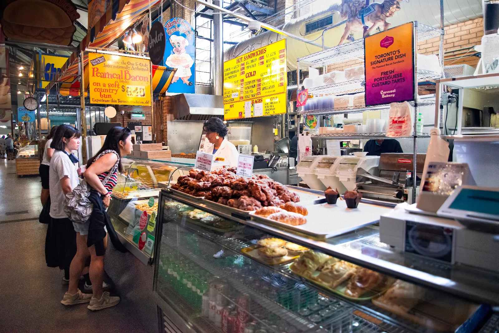 Food counters, colourful signs and visitors shopping inside Toronto’s St. Lawrence Market