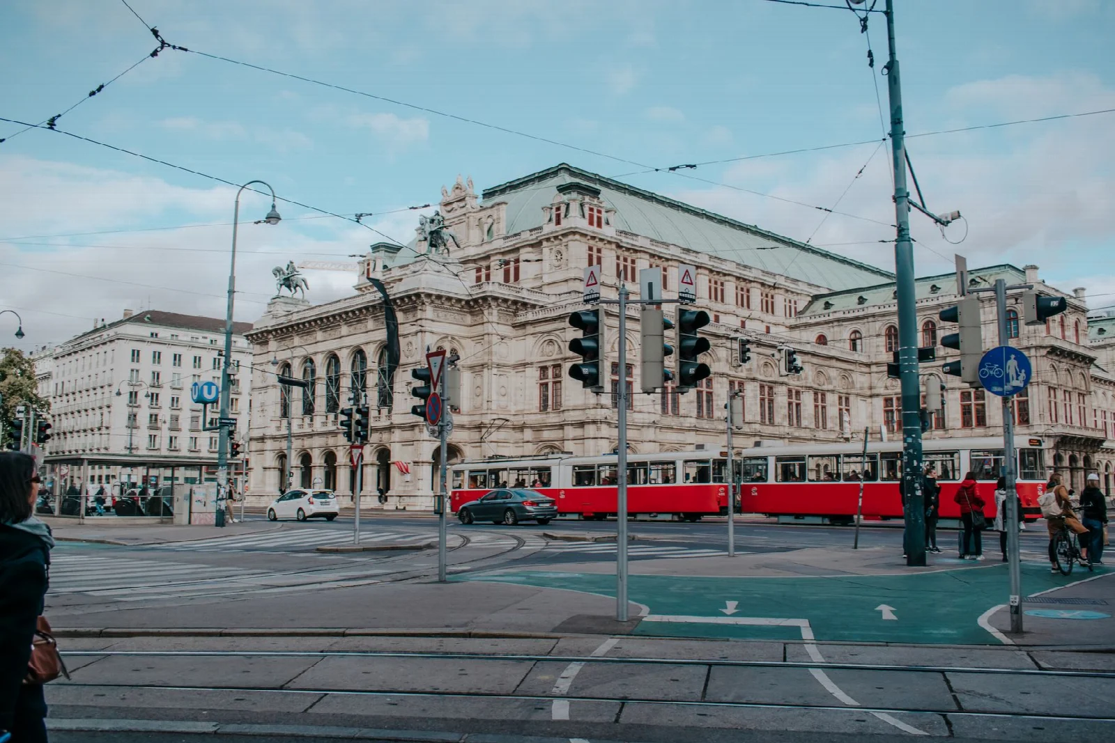 A red tram and city traffic passing the Vienna State Opera
