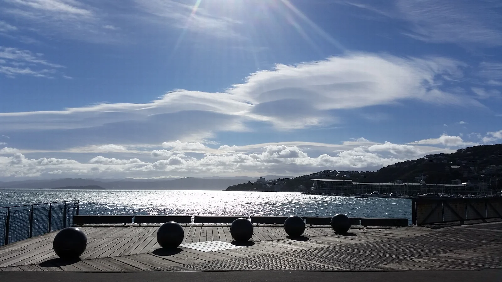 A timber platform with five round objects on Wellington’s waterfront, with shining water and layered clouds